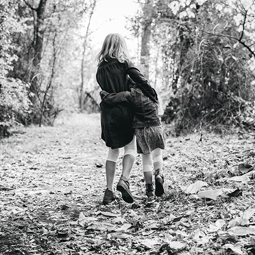 Young girls walking arm in arm along a woodland path